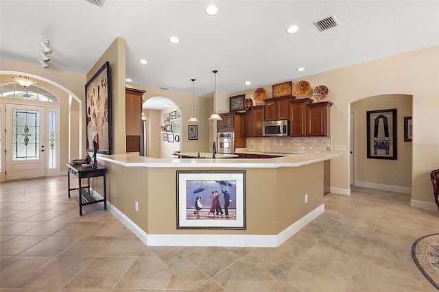 kitchen featuring tasteful backsplash, pendant lighting, a textured ceiling, a breakfast bar, and appliances with stainless steel finishes