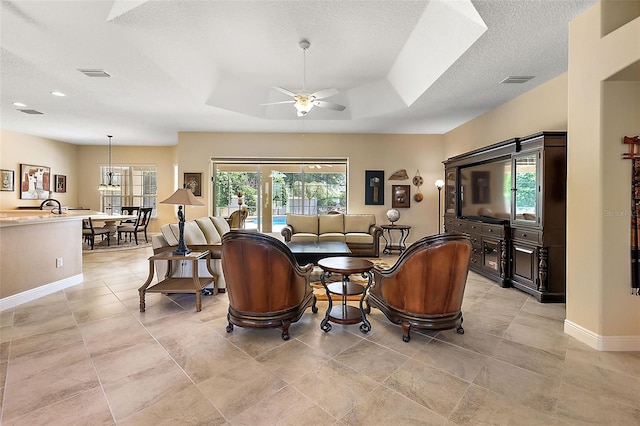 living room with a raised ceiling, ceiling fan, and a textured ceiling