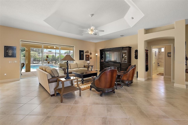 living room with a raised ceiling, ceiling fan, light tile patterned floors, and a textured ceiling