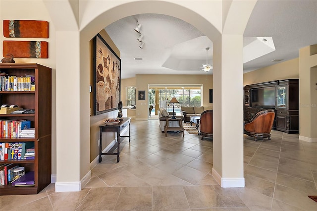 hallway featuring a tray ceiling, track lighting, light tile patterned flooring, and a textured ceiling