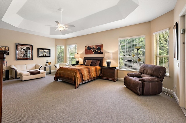 carpeted bedroom with a raised ceiling and ceiling fan