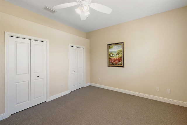 unfurnished bedroom with dark colored carpet, ceiling fan, and multiple closets