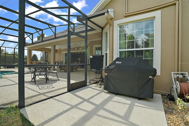 view of patio with ceiling fan, a grill, and glass enclosure