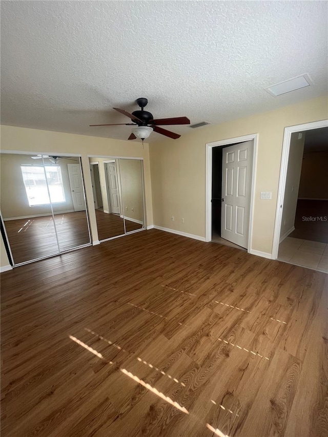 unfurnished bedroom featuring multiple closets, ceiling fan, a textured ceiling, and hardwood / wood-style flooring