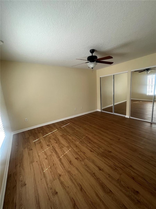 unfurnished bedroom featuring two closets, a textured ceiling, hardwood / wood-style flooring, and ceiling fan