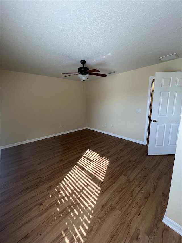 empty room with ceiling fan, dark wood-type flooring, and a textured ceiling