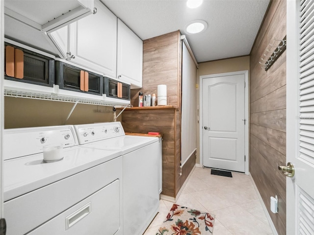 laundry room featuring cabinets, wooden walls, washing machine and dryer, light tile patterned floors, and a textured ceiling