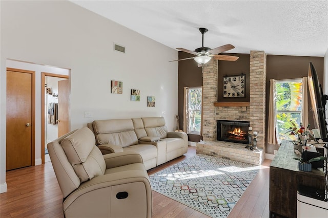 living room with a brick fireplace, a textured ceiling, light hardwood / wood-style flooring, and ceiling fan