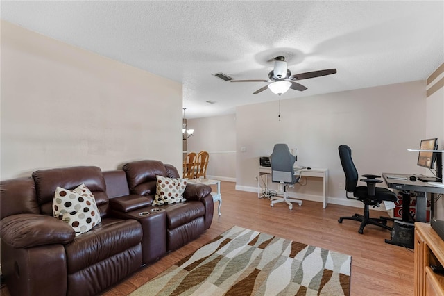 office space with ceiling fan with notable chandelier, a textured ceiling, and light hardwood / wood-style flooring