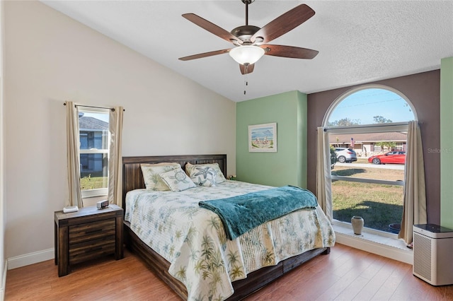 bedroom featuring wood-type flooring, a textured ceiling, multiple windows, and ceiling fan