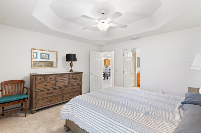 bedroom with a tray ceiling, ensuite bathroom, ceiling fan, and light carpet