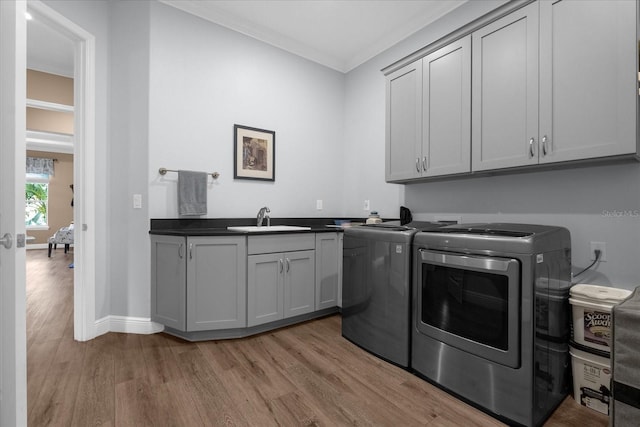 laundry room with sink, cabinets, washing machine and dryer, light hardwood / wood-style flooring, and ornamental molding