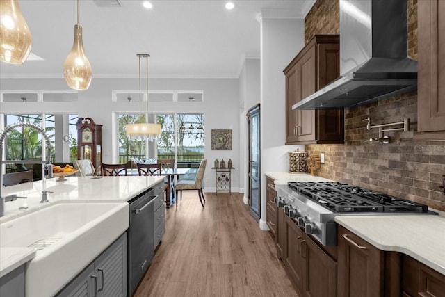 kitchen with wall chimney range hood, stainless steel appliances, hanging light fixtures, and ornamental molding