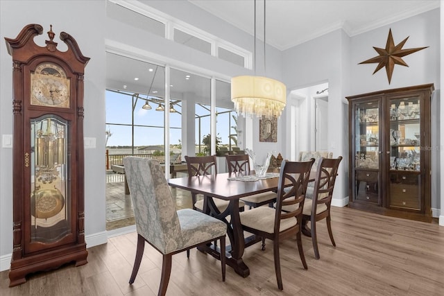 dining space with hardwood / wood-style flooring, a notable chandelier, ornamental molding, and a high ceiling