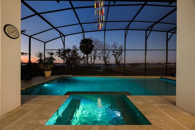 pool at dusk featuring an in ground hot tub, a patio area, and a lanai