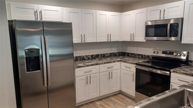 kitchen with white cabinetry, stainless steel appliances, and dark stone counters