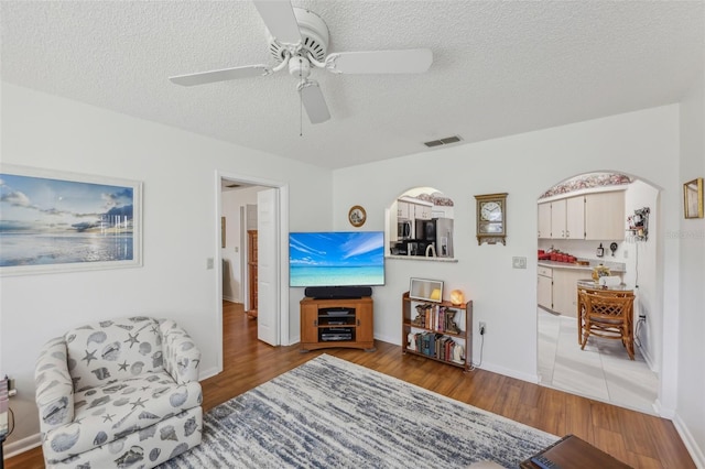 living room with ceiling fan, light wood-type flooring, and a textured ceiling