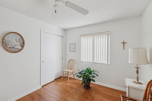 living area featuring ceiling fan, wood-type flooring, and a textured ceiling