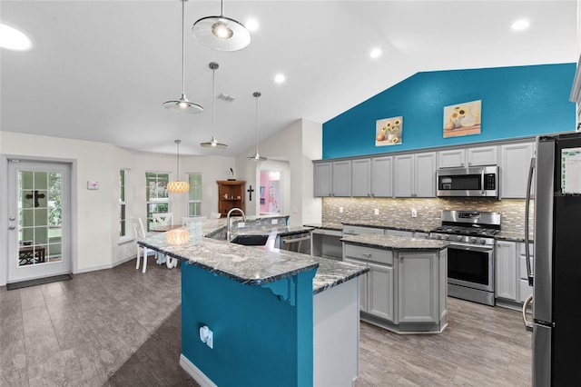 kitchen featuring backsplash, pendant lighting, appliances with stainless steel finishes, and a center island with sink