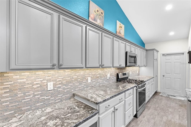 kitchen featuring gray cabinets, stainless steel appliances, decorative backsplash, lofted ceiling, and dark stone countertops