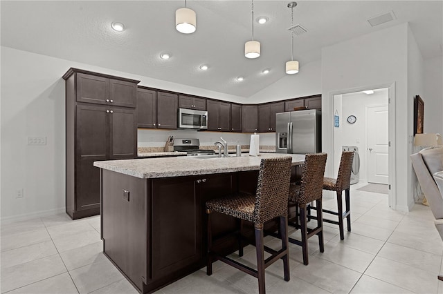 kitchen with dark brown cabinets, stainless steel appliances, hanging light fixtures, and a kitchen island with sink