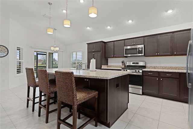 kitchen with hanging light fixtures, light stone counters, an island with sink, a breakfast bar, and appliances with stainless steel finishes