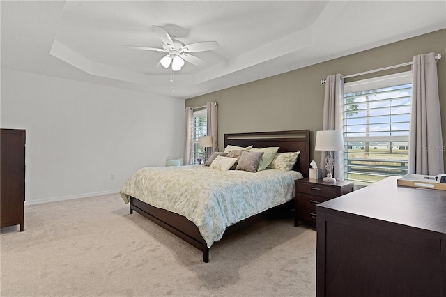 carpeted bedroom with ceiling fan, a raised ceiling, and multiple windows