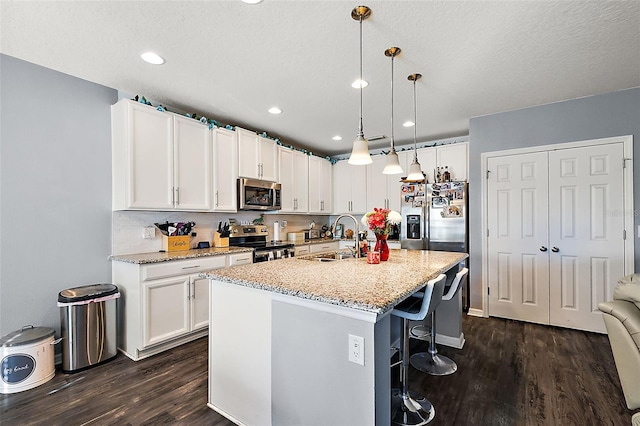 kitchen featuring pendant lighting, sink, white cabinets, stainless steel appliances, and a center island with sink