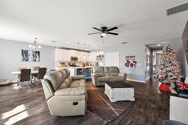 living room with dark hardwood / wood-style flooring, ceiling fan with notable chandelier, and a textured ceiling