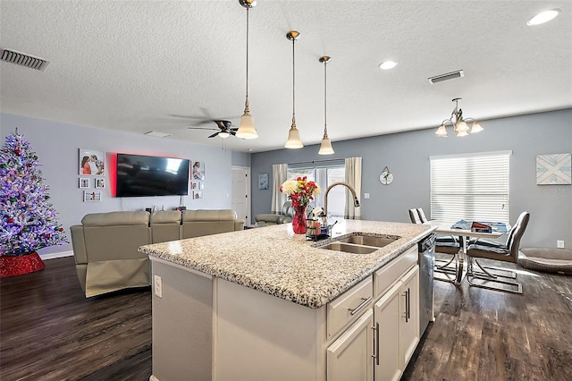 kitchen with pendant lighting, sink, stainless steel dishwasher, light stone countertops, and a center island with sink