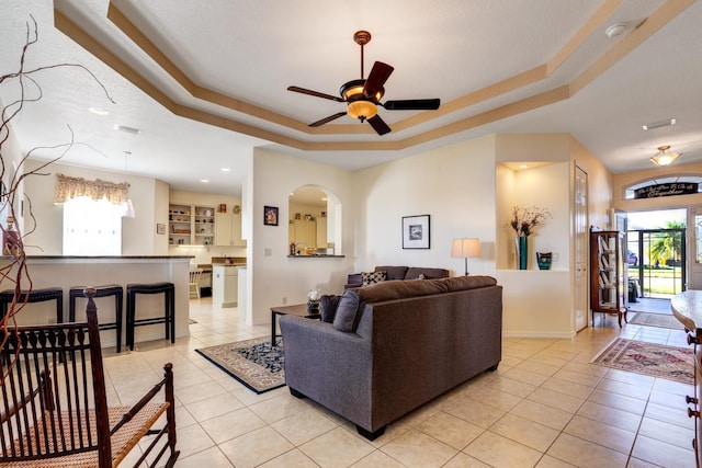 living room featuring plenty of natural light, ceiling fan, light tile patterned floors, and a tray ceiling