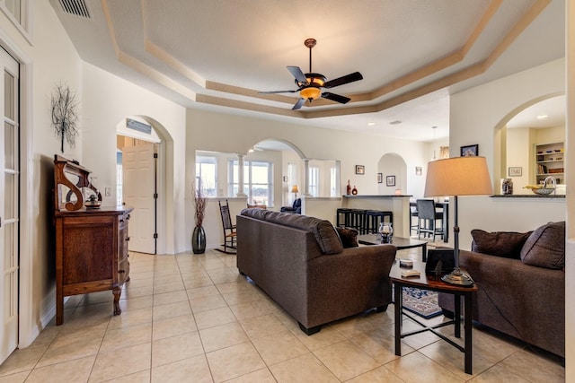 living room with ceiling fan, a raised ceiling, and light tile patterned floors