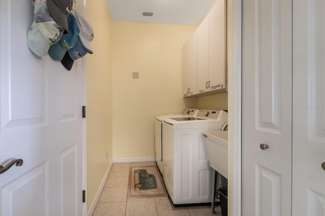 clothes washing area with washer and dryer, light tile patterned floors, and cabinets