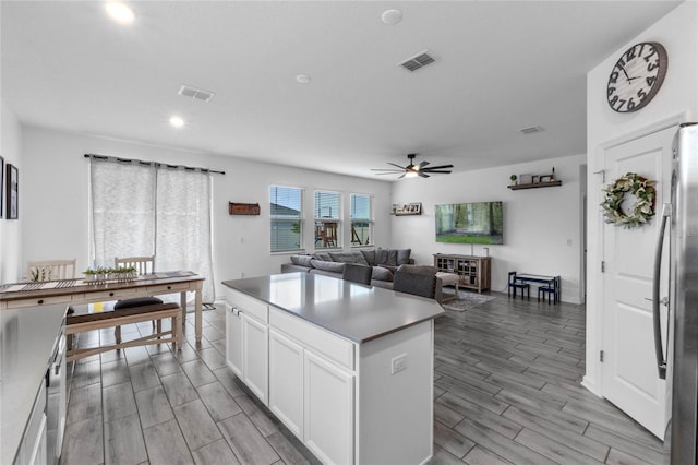 kitchen with stainless steel refrigerator, white cabinetry, ceiling fan, a kitchen island, and light wood-type flooring