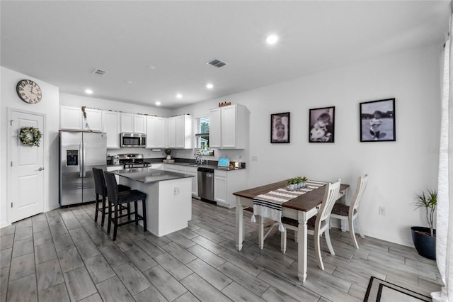 kitchen with a breakfast bar, a kitchen island, light hardwood / wood-style floors, white cabinetry, and stainless steel appliances