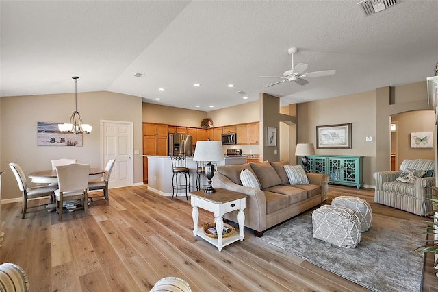 living room with ceiling fan with notable chandelier, light hardwood / wood-style floors, and vaulted ceiling