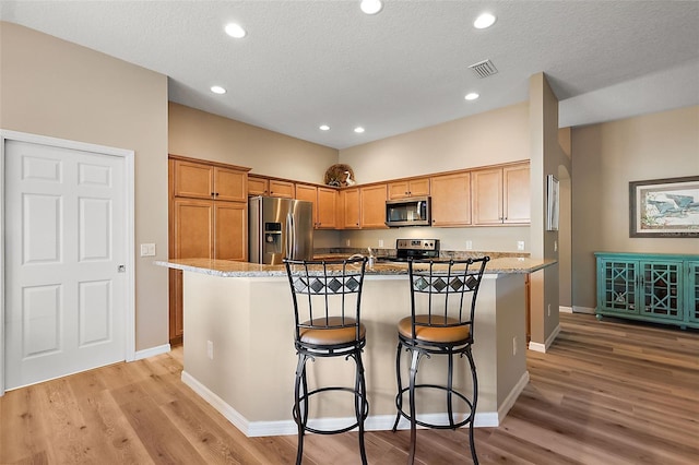 kitchen with light stone countertops, stainless steel appliances, and a kitchen island with sink