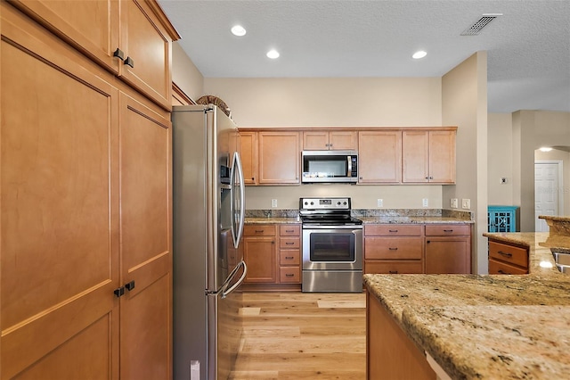 kitchen with a textured ceiling, light stone countertops, stainless steel appliances, and light hardwood / wood-style flooring