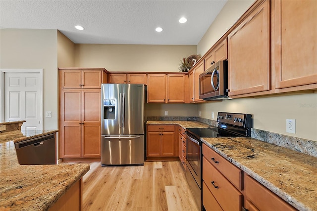 kitchen featuring light stone countertops, light wood-type flooring, a textured ceiling, and appliances with stainless steel finishes