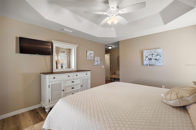 bedroom with wood-type flooring, a raised ceiling, and ceiling fan