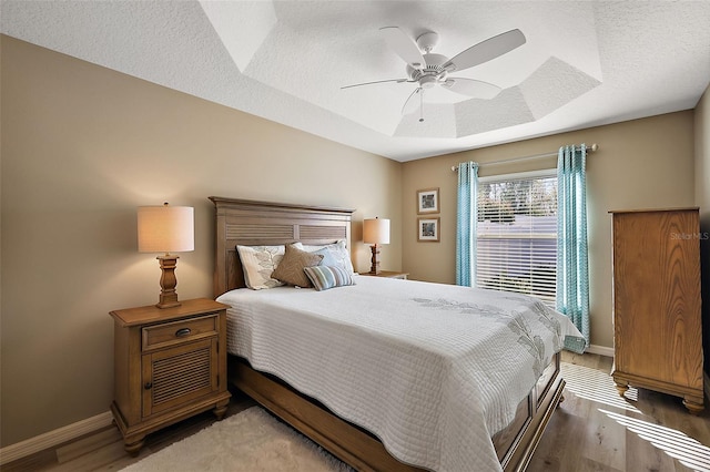 bedroom featuring a textured ceiling, hardwood / wood-style flooring, ceiling fan, and a tray ceiling