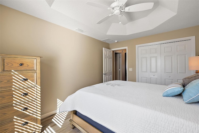 bedroom with hardwood / wood-style floors, a raised ceiling, a closet, and ceiling fan