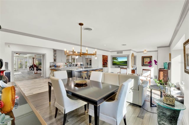 dining space with an inviting chandelier, ornamental molding, and light wood-type flooring