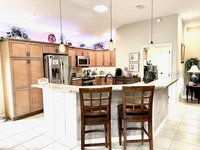 kitchen with a kitchen island with sink, a kitchen breakfast bar, light tile patterned floors, decorative light fixtures, and stainless steel appliances