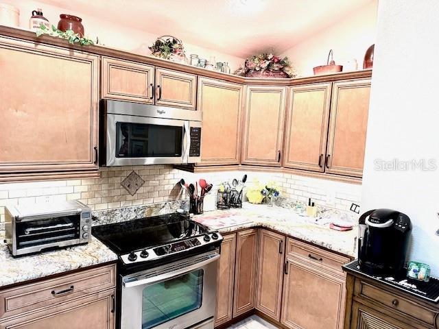 kitchen with light stone countertops, stainless steel appliances, tasteful backsplash, and lofted ceiling