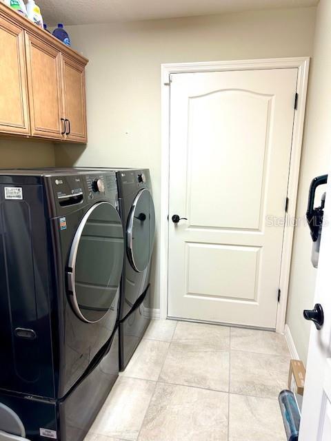 laundry room featuring washer and dryer, cabinets, and light tile patterned floors