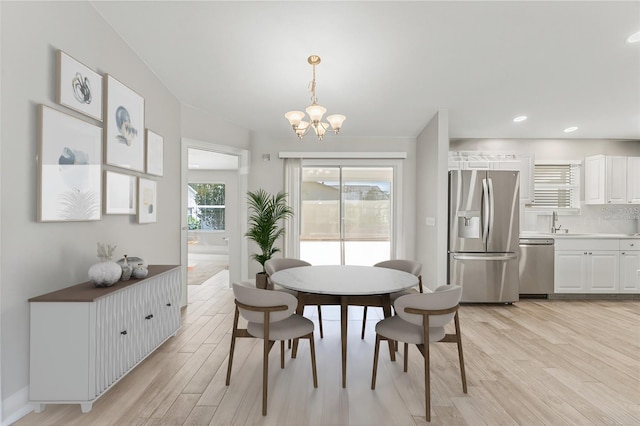 dining area with sink, light hardwood / wood-style floors, and an inviting chandelier