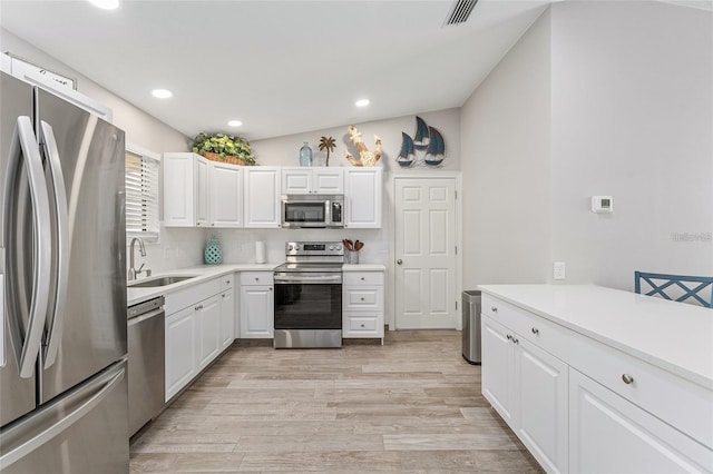 kitchen featuring sink, backsplash, lofted ceiling, white cabinets, and appliances with stainless steel finishes