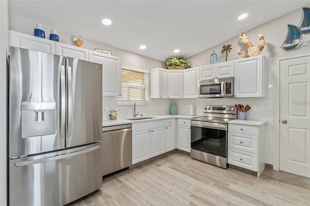 kitchen with white cabinets, sink, decorative backsplash, light wood-type flooring, and appliances with stainless steel finishes