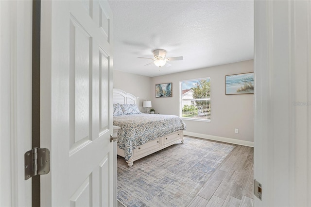 bedroom with a textured ceiling, light hardwood / wood-style flooring, and ceiling fan